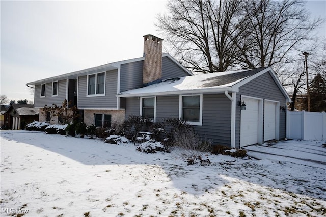 snow covered property featuring a chimney, fence, a detached garage, and brick siding