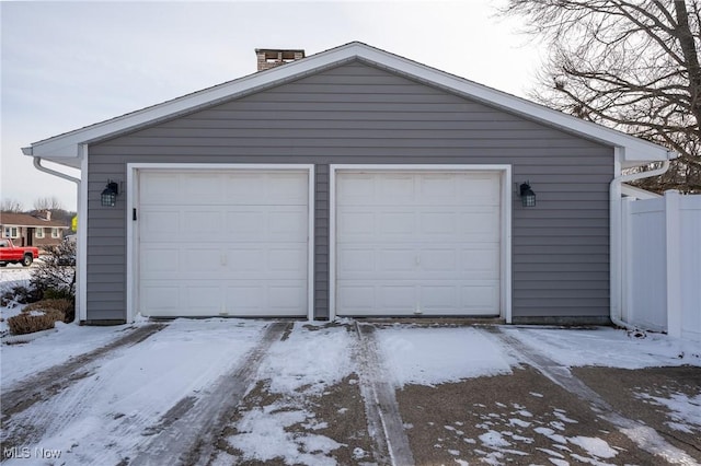 snow covered garage with a garage and fence