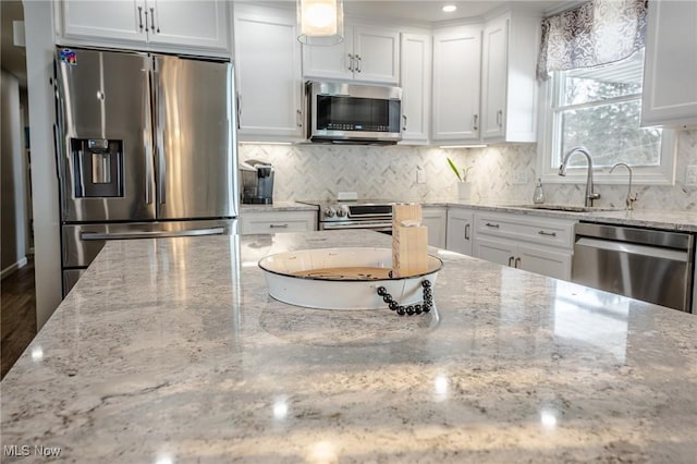 kitchen featuring tasteful backsplash, appliances with stainless steel finishes, light stone counters, white cabinetry, and a sink