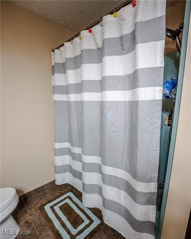 bathroom featuring a shower with curtain, stone finish flooring, a textured ceiling, and toilet