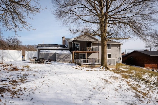 snow covered house featuring a balcony, a chimney, and fence