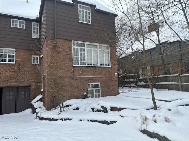 snow covered house with a garage, brick siding, and fence