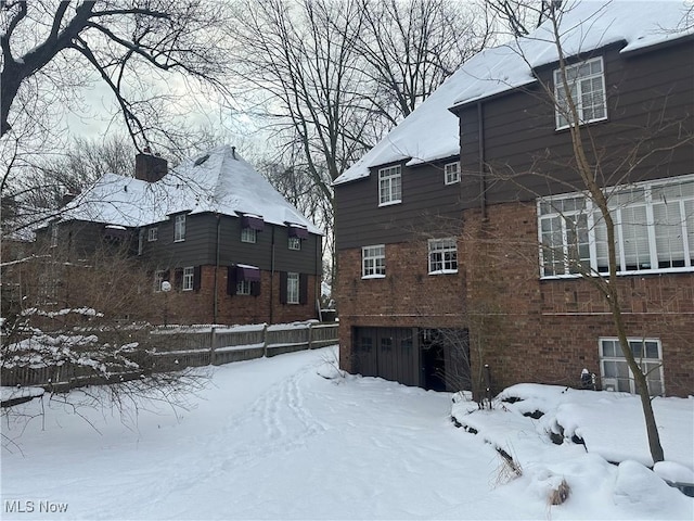 view of snowy exterior featuring a garage and brick siding