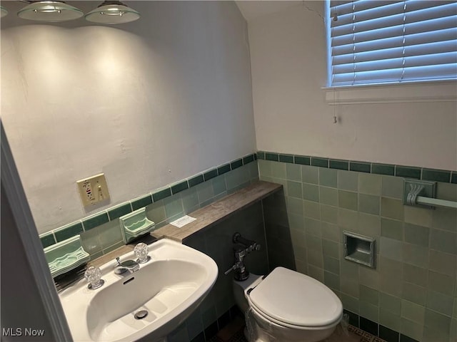 half bath with a wainscoted wall, a sink, tile walls, and toilet