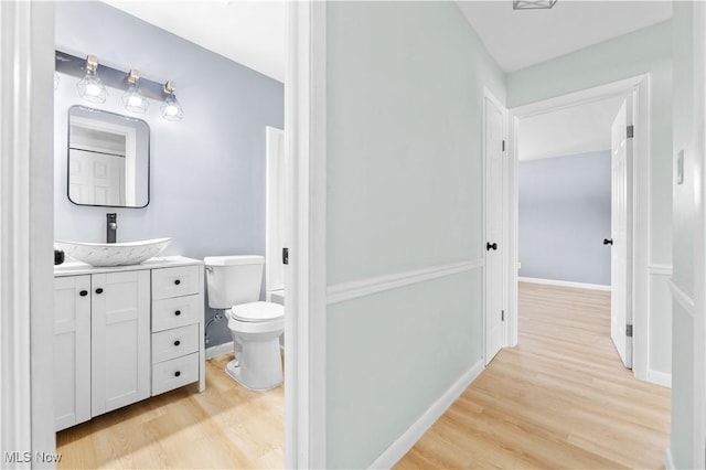 half bathroom featuring toilet, vanity, baseboards, and wood finished floors