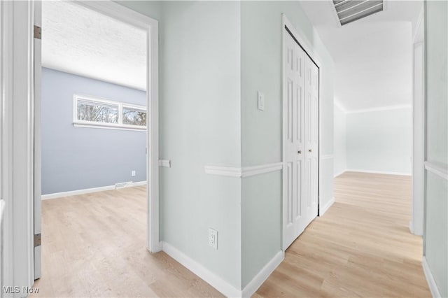 hall featuring a textured ceiling, light wood-type flooring, visible vents, and baseboards