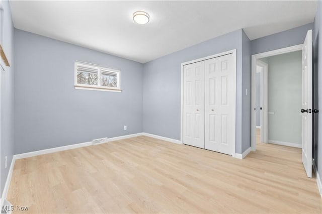 unfurnished bedroom with light wood-style flooring, visible vents, baseboards, and a closet