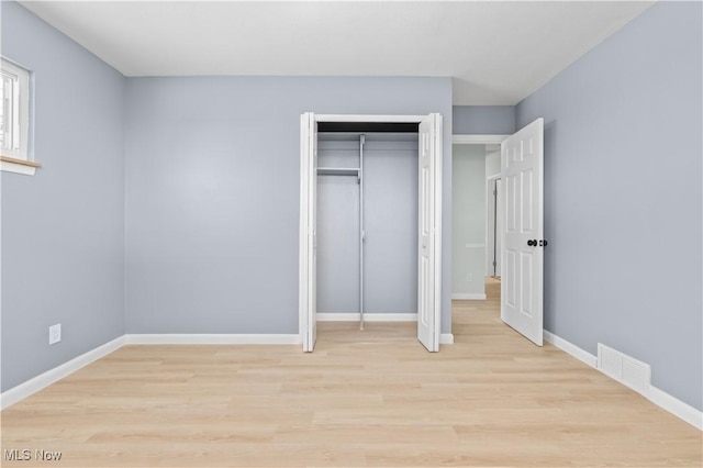 unfurnished bedroom featuring light wood-type flooring, baseboards, visible vents, and a closet