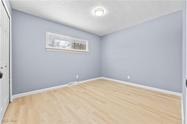 unfurnished room with light wood-style floors, baseboards, visible vents, and a textured ceiling