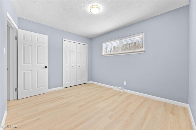 unfurnished bedroom featuring a textured ceiling, light wood-style flooring, visible vents, baseboards, and a closet