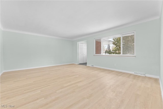 spare room with ornamental molding, light wood-style flooring, visible vents, and baseboards