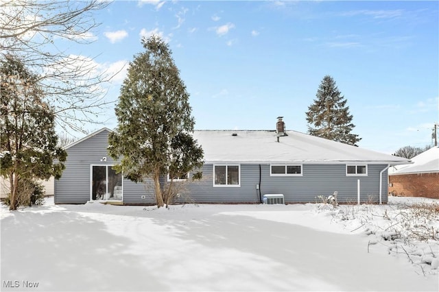 snow covered property featuring a chimney and central AC