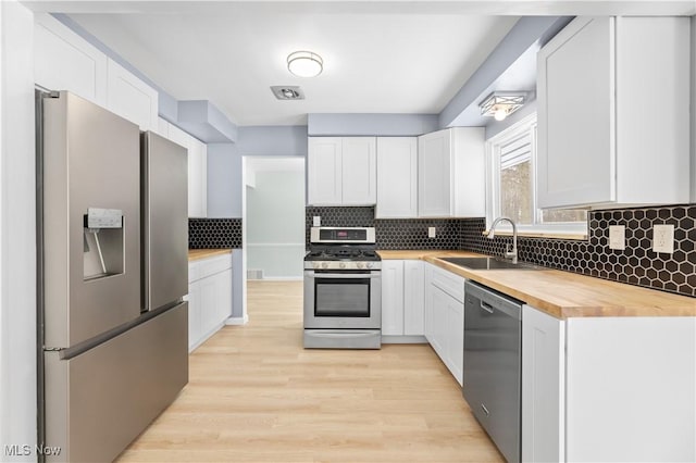 kitchen featuring stainless steel appliances, tasteful backsplash, white cabinetry, a sink, and wood counters