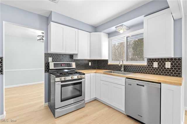 kitchen with butcher block counters, appliances with stainless steel finishes, white cabinets, and a sink