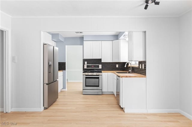 kitchen featuring appliances with stainless steel finishes, butcher block countertops, a sink, and white cabinetry