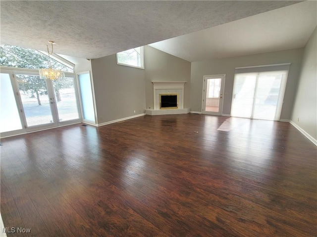 unfurnished living room with dark wood-style flooring, a notable chandelier, a fireplace with raised hearth, vaulted ceiling, and baseboards