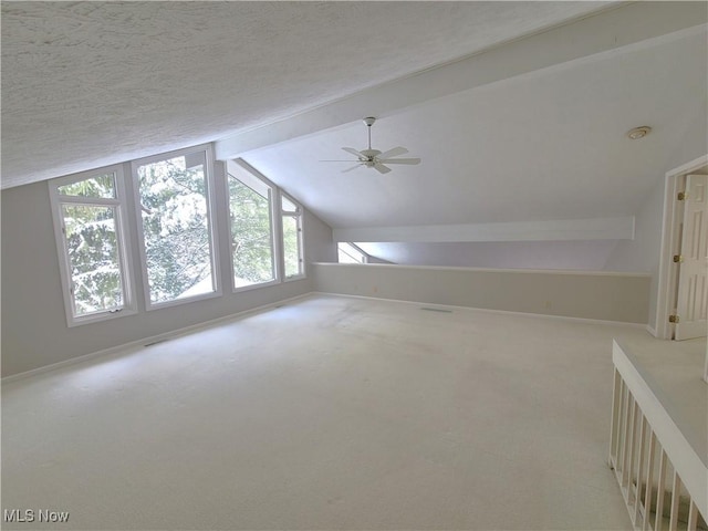 additional living space featuring lofted ceiling with beams, ceiling fan, a textured ceiling, and carpet flooring