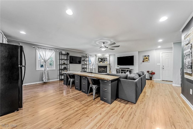 living area with ceiling fan, light wood-type flooring, a fireplace, and baseboards