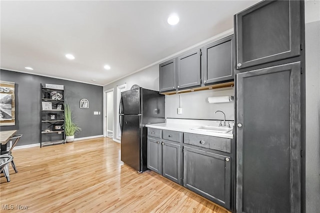 kitchen featuring light countertops, light wood-style flooring, freestanding refrigerator, a sink, and baseboards