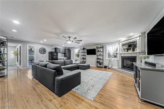 living area featuring baseboards, a glass covered fireplace, ceiling fan, light wood-style floors, and recessed lighting