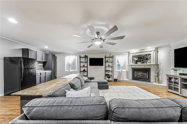 living room featuring ceiling fan, plenty of natural light, a glass covered fireplace, and light wood-style flooring