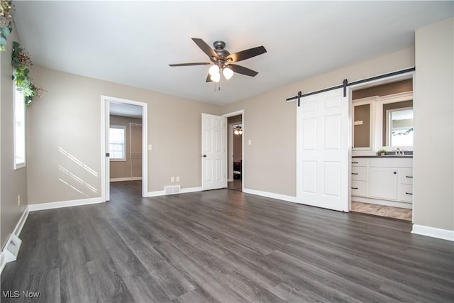 unfurnished bedroom with a barn door, visible vents, dark wood finished floors, and baseboards