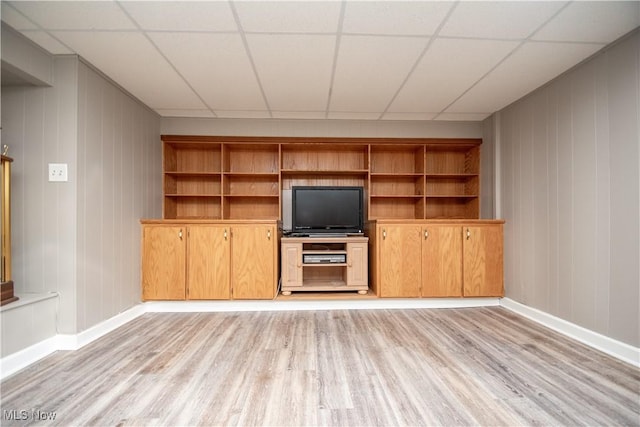 unfurnished living room with light wood-type flooring, a paneled ceiling, and baseboards