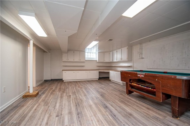 below grade area with light wood-style floors, baseboards, and built in desk