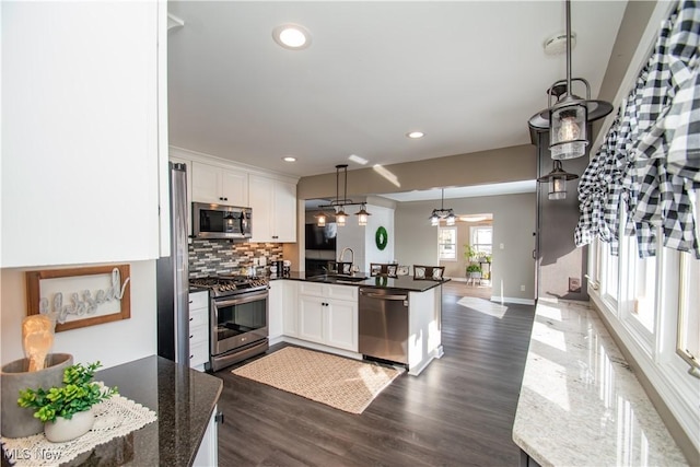 kitchen featuring pendant lighting, stainless steel appliances, white cabinets, a sink, and a peninsula