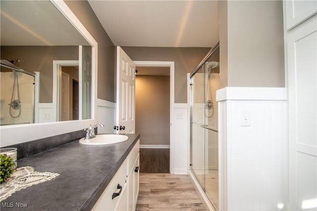 full bath with a wainscoted wall, a stall shower, wood finished floors, and vanity