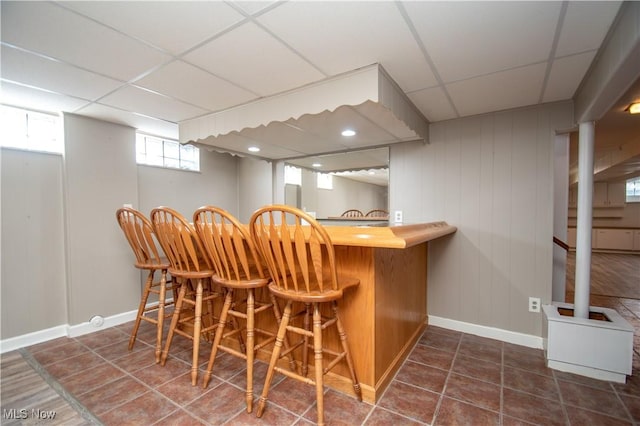 bar with a dry bar, dark tile patterned floors, baseboards, and a paneled ceiling