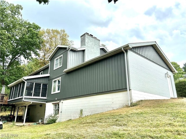 view of property exterior with a yard, a chimney, and a sunroom