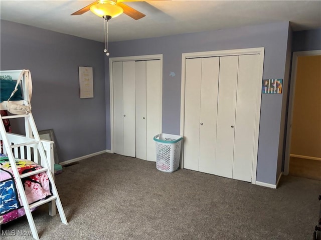 unfurnished bedroom with a ceiling fan, baseboards, dark colored carpet, and two closets