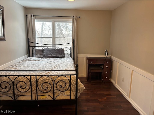 bedroom with a decorative wall, dark wood-type flooring, and wainscoting