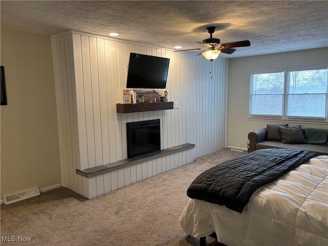 bedroom with carpet, visible vents, a ceiling fan, a glass covered fireplace, and a textured ceiling