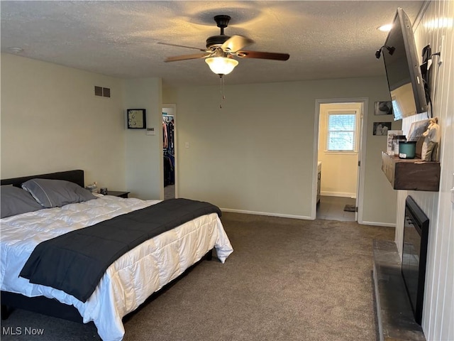 bedroom with a textured ceiling, visible vents, baseboards, a spacious closet, and dark carpet