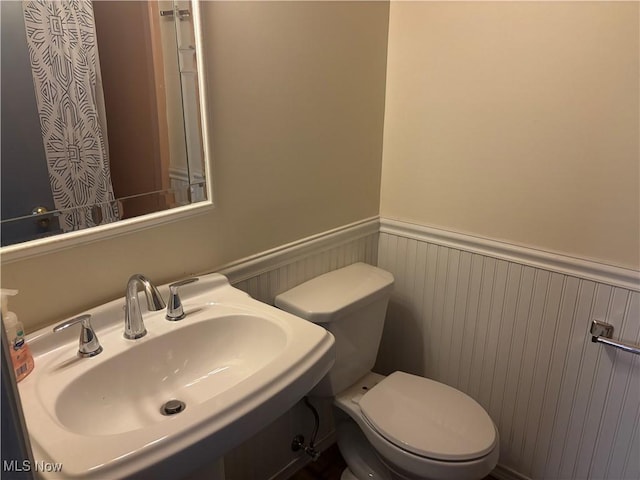 bathroom featuring a wainscoted wall, a sink, and toilet