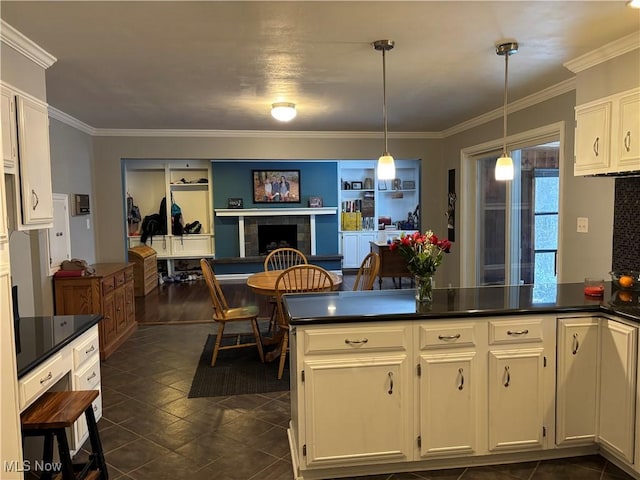 kitchen featuring dark countertops, decorative light fixtures, a tiled fireplace, and white cabinetry