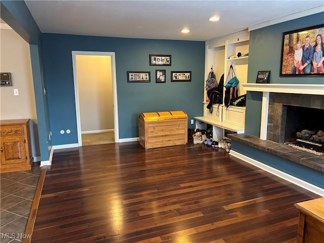 interior space featuring dark wood-style floors, baseboards, a tiled fireplace, and recessed lighting