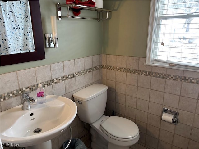 bathroom with a wainscoted wall, a sink, toilet, and tile walls