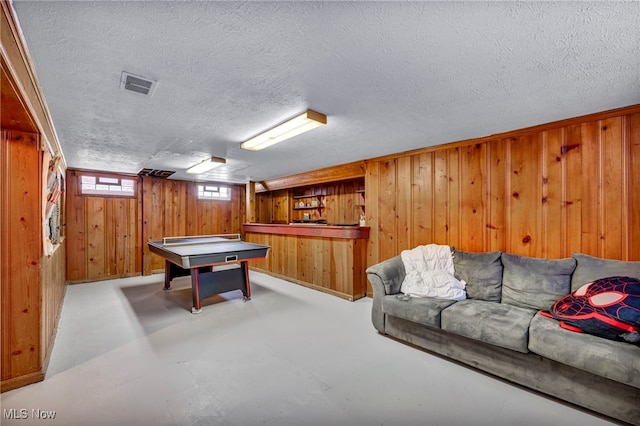 rec room with wooden walls, concrete floors, visible vents, and a textured ceiling