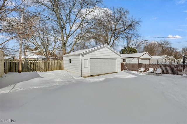 snow covered garage featuring a garage and fence