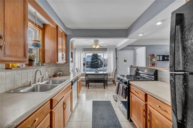 kitchen with brown cabinets, light countertops, decorative backsplash, a sink, and black appliances