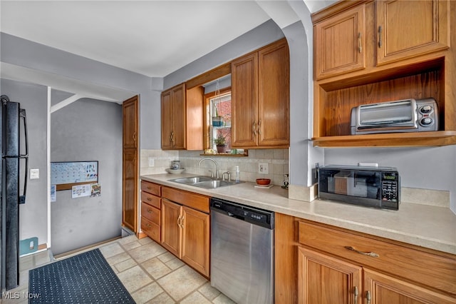 kitchen featuring light countertops, decorative backsplash, brown cabinetry, a sink, and black appliances