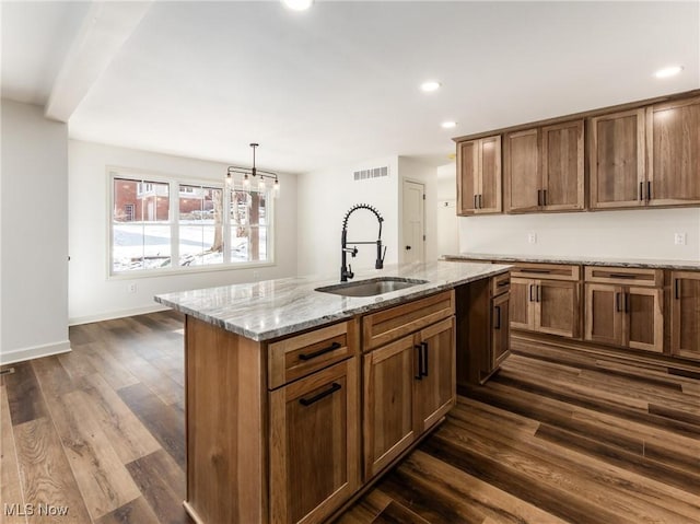 kitchen with pendant lighting, visible vents, brown cabinetry, a kitchen island with sink, and a sink