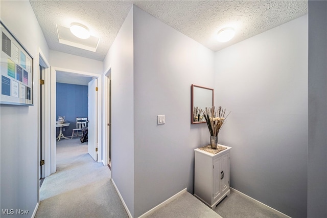 hallway featuring baseboards, a textured ceiling, attic access, and light colored carpet