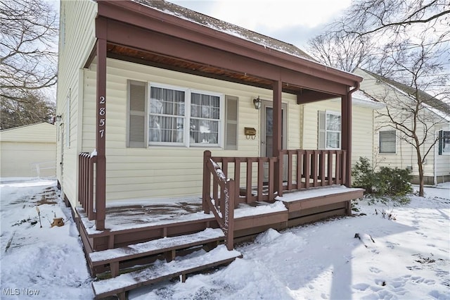 snow covered property entrance with a detached garage