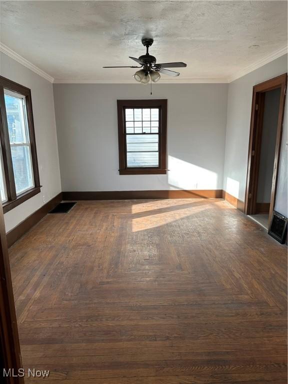 empty room featuring a textured ceiling, a ceiling fan, visible vents, baseboards, and crown molding