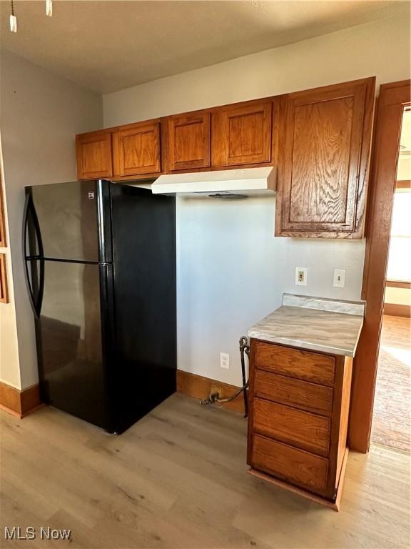 kitchen featuring light countertops, light wood-type flooring, freestanding refrigerator, and brown cabinets