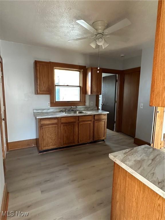 kitchen featuring brown cabinets, light countertops, light wood-style flooring, a sink, and baseboards